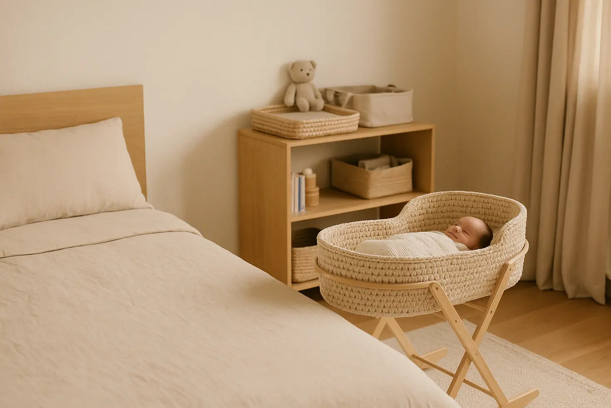 A crochet Moses basket beside a bed in a calm, organised newborn room.