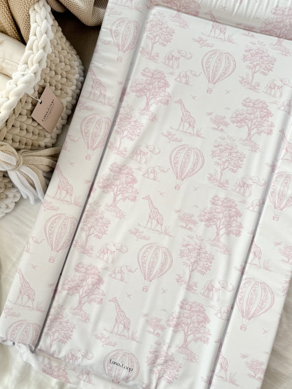 Baby changing mat in pink toile print beside a crochet basket